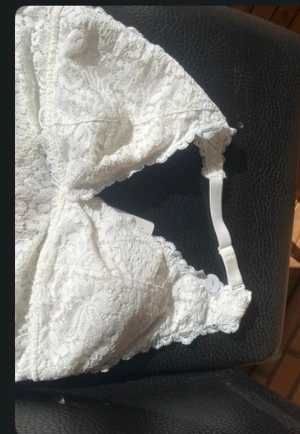 Vit spetsig bh - Säljer en vit bh i spets med fina blommiga detaljer. Bh:n är ärmlös och har justerbara axelband för perfekt passform. Perfekt för att skapa en romantisk och trendig look. Storlek M