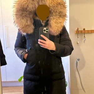 Svart dunjacka med päls från Cedrico - Säljer en svart dunjacka från Cedrico med stor fluffig päls runt huvan. Jackan har flera fickor med dragkedja, justerbara detaljer i midjan och långa ärmar. Perfekt för kalla vinterdagar och har en riktigt snygg, urban vibe. Nypris 8499