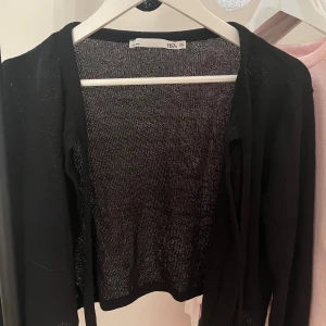 Svart tunn kofta med knyt XS - Svart, tunn och lättstickad kofta från 157 i storlek XS. Modellen är croppad och har långa ärmar samt knytband framtill vid halsen. Perfekt att slänga över ett linne eller klänning. Upplevs ej genomskinlig på. Aldrig använts. Nypris 150/200kr 