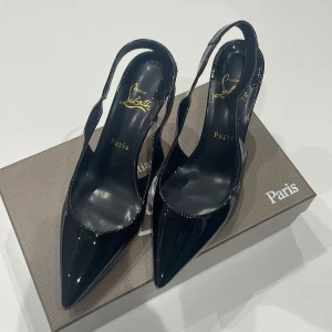 Svarta pumps från Christian Louboutin - Säljer ett par svarta pumps från Christian Louboutin med glansig finish och ikonisk röd sula. Skorna har spetsig tå, hög klack och öppen häl med slingback-rem. Tillverkade i lackat skinn för en lyxig och edgy look. Perfekta för dig som vill sticka ut.