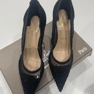 Svarta pumps från Christian Louboutin - Snygga svarta pumps med spetsig tå från Christian Louboutin. Skorna har meshpartier med prickigt mönster, glittriga detaljer och klassisk röd sula. Klacken är smal och elegant, och materialet är en mix av mesh och mocka. Perfekt för dig som vill sticka ut.