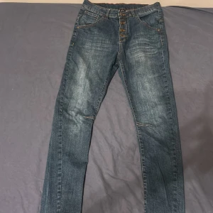 Blå jeans från Denim Original - Snygga blå jeans från Denim Original med klassisk femficksdesign och knappgylf. Jeansen har en rak passform och subtila slitningar framtill för en cool look. Perfekta för dig som gillar tidlös stil och bekvämt material.