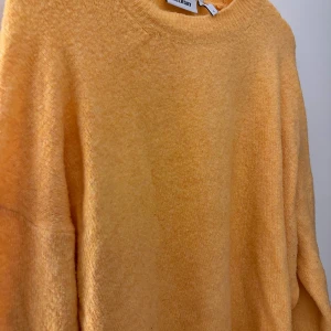 Gul stickad tröja från Weekday - Mysig orangegul stickad tröja från Weekday i storlek L. Tröjan har en rund halsringning, långa ärmar och en avslappnad passform. Perfekt för lager-på-lager och enkel att styla med jeans eller kjol.