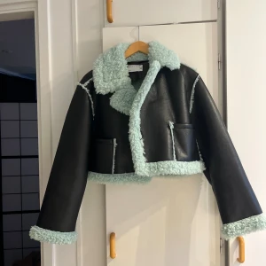Svart teddyjacka med mintgrön fuskpäls - Cool croppad teddyjacka från ASOS DESIGN i svart med mintgrön fuskpäls på krage, ärmslut och nederkant. Jackan har två fickor fram och markerade sömmar i samma mintgröna färg. Perfekt statement-plagg för dig som vill sticka ut.