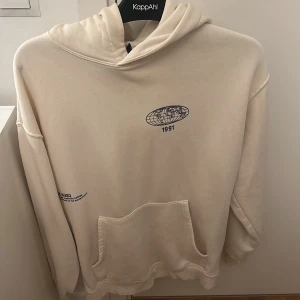 Beige hoodie med tryck från KappAhl - Säljer en beige hoodie med blått tryck fram och bak. Tröjan har huva, stor magficka och lång ärm. 