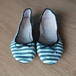 Randiga ballerinaskor med rosett - Snygga ballerinaskor med marinblå och vita ränder, rund tå och liten rosett framtill. Skorna har en mjuk textil ovandel och platt sula, perfekta för dig som gillar enkel och stilren design med en twist.