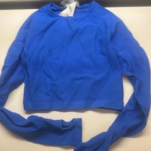 Blå croppad långärmad träningströja - Snygg blå croppad långärmad träningströja med ribbade detaljer längs sidorna och ärmarna. 