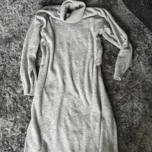 Grå stickad långklänning Lindex - Mysig grå stickad långklänning från Lindex med polokrage och långa ärmar. Klänningen har en enkel, rak passform och är tillverkad i mjukt stickat material som känns skönt mot huden. Perfekt för dig som gillar stilren och comfy look.