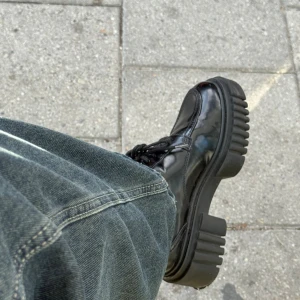 Svarta chunky boots med snörning - Säljer ett par svarta boots med riktigt chunky plattformsula och snörning. Skorna har en glansig finish i skinn och rund tå. Perfekta för dig som vill ha en edgy och modern look med extra höjd. Snygga detaljer och grov sula som sticker ut.