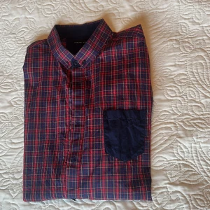 Rutig skjorta från Selected Homme XL - Snygg rutig skjorta från Selected Homme i storlek XL. Skjortan har ett klassiskt mönster i mörkblått och rött med en marinblå bröstficka, långärmade ärmar. 