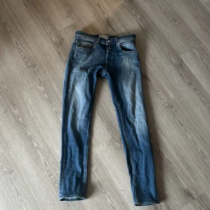 Blå Replay Anbass jeans slim fit - Snygga blå Replay Anbass jeans med slim passform och klassisk femficksdesign. Jeansen har en lätt tvättad look med detaljerade sömmar på bakfickorna. Passar dig som gillar en modern och smal siluett.