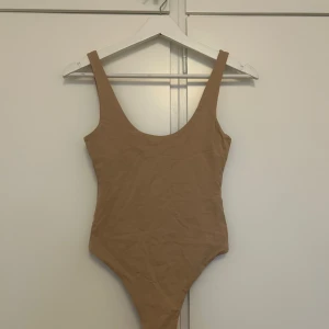 Beige body från BikBok XS - Snygg beige body från BikBok i storlek XS. Modellen har breda axelband och en djup rundad urringning fram. Materialet är mjukt och stretchigt. Endast testad på aldrig använd annars.🤎