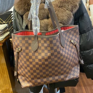 Lara  shoppingväska - Snygg och rymlig shoppingväska . Väskan är brun och beige med rödrandigt foder, har långa handtag och detaljer i mörkbrunt skinn. Perfekt för dig som vill ha både stil och funktion.