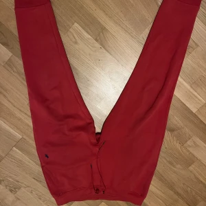 Röda mjukisbyxor med snörning - Snygga röda mjukisbyxor med elastisk midja och snörning framtill. Byxorna har en bakficka och ribbade muddar vid bensluten. Perfekta för chill eller träning, mjukt material och relaxed passform.