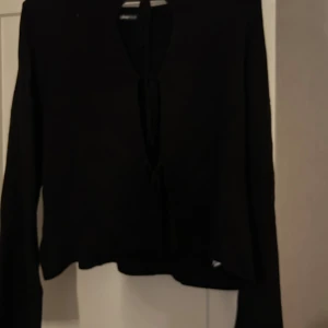 Svart omlottopp från Gina Tricot - Svart omlottopp från Gina Tricot med långa ärmar och snygg knytning framtill. Croppad passform som ger en trendig look. Perfekt att styla med höga jeans eller kjol. Materialet känns mjukt och lätt mot huden.