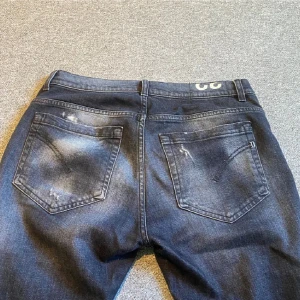 Mörkblå Dondup jeans med slitningar - Säljer ett par mörkblå jeans från Dondup i storlek 32. Jeansen har snygga slitningar och en tvättad look, klassisk femficksmodell och smal passform. Perfekta för dig som gillar en lite ruffare stil.
