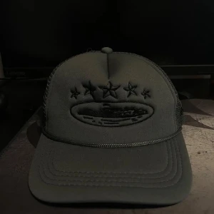 Svart truckerkeps med stjärnor - Svart truckerkeps med broderade stjärnor framtill och mesh på sidorna och bak. Justerbar snapback för perfekt passform. Snyggt broderad logga och detaljer i svart ton. Perfekt för dig som gillar streetwear och vill ha en stilren look.