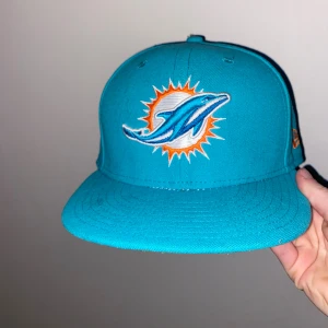 Turkos Miami Dolphins keps från New Era - Snygg turkos keps från New Era med Miami Dolphins-logga broderad framtill och NFL-märke baktill. Klassisk flatbrim och orange detaljer på sidan. Pris går att diskutera 