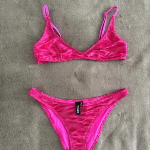 Rosa bikini från Triangl, strl M - Snygg rosa bikini från Triangl i storlek M. Bikinin har en vågigt material men är enfärgad, rosa. Toppen har justerbara axelband och spänne i ryggen. Inga defekter och inte mycket använd💕