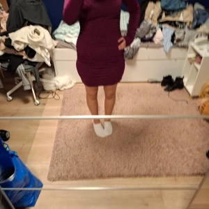 Glittrig vinröd kortklänning - Säljer en snygg vinröd kortklänning med glittrigt material och långärmad design. Klänningen har en tight passform och är perfekt klubboutfit.. Den har lätt rynkade detaljer på sidorna och är superstretchig. Passar dig som gillar att klä dig trendigt och vågar ta plats.