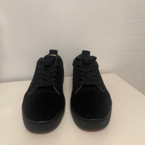 BUD! - Säljer ett par svarta Christian Louboutins i mjuk mocka med klassisk röd sula och snygga svarta snören. Insidan är beige och har Paris-tryck. Skorna har rund tå och platt sula, perfekt för dig som gillar exklusiv stil med en twist.