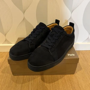 Svarta sneakers från Christian Louboutin - Snygga mörkblå  sneakers från Christian Louboutin med klassisk rund tå och platt sula. Skorna har mörkblå mocka på ovansidan, mörkblå snören och en ikonisk röd undersida. Insidan är fodrad i beige skinn för extra komfort. Perfekt för dig som gillar exklusiv stil.