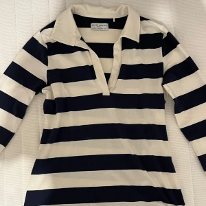 Randig pikétröja Holly & Whyte  - Snygg randig pikétröja från Holly & Whyte by Lindex i marinblått och vitt. Tröjan har klassisk krage, v-ringning och långa ärmar. Perfekt för en preppy look och tillverkad i mjuk bomull som känns skön mot huden.