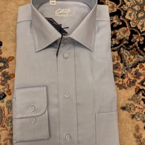 Ljusblå skjorta från Oscar, strl 43 - Klassisk ljusblå skjorta från Oscar i 100% bomull. Skjortan har diskreta diagonala ränder, lång ärm, knappar framtill och bred krage. Perfekt för dig som gillar stilrena och snygga skjortor med en clean look.