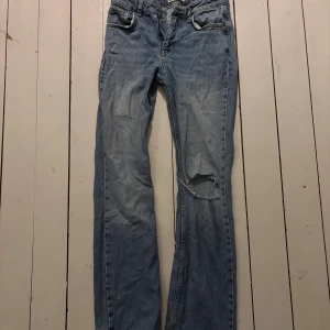 Blå jeans med hål på knät - Säljer ett par ljusblå jeans med klassisk femficksdesign och slitning på ena knät. Jeansen har rak passform och är tillverkade i mjukt denimtyg. Perfekt för dig som gillar en avslappnad och cool stil.