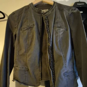 Grå jeansjacka från Esprit - Snygg grå jeansjacka från Esprit med coola sömmar och dekorativ kant längs öppningen. Jackan har lång ärm, rund hals och fyra fickor framtill. Perfekt att slänga över en hoodie eller t-shirt för en chill look.