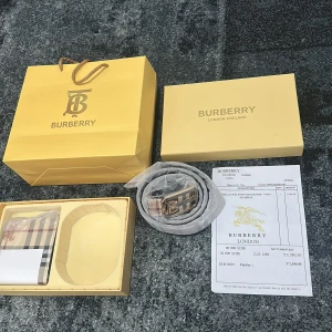 Burberry rutigt skärp med B-spänne - Säljer ett snyggt Burberry bälte i klassiskt rutig design med beige, svart och röd färg. Bältet har ett stilrent metallspänne med Burberrys B-logga i silver. Materialet är exklusivt skinn och bältet kommer med originalförpackning och certifikat.