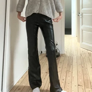 Utsvängda skinnbyxor  - Snygga svarta byxor i skinnimitation med utsvängda passform . Materialet är glansigt och ger en cool vibe, perfekt för dig som gillar att sticka ut med din stil.