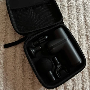 Mini massage pistol  med tillbehör - Kompakt massagepistol i svart med flera utbytbara munstycken och praktiskt fodral. Laddas via USB-C och har flera hastighetslägen. Perfekt för muskelavslappning hemma eller på resan. Mycket fint skick, inga synliga defekter eller slitage. Laddare ingår ej.