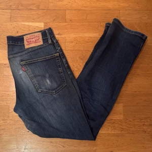 Levi's 514 mörkblå jeans straight fit - Säljer ett par Levi's 514 jeans i mörkblå tvätt med klassisk straight fit. Jeansen är påväg att få ett litet hål vid baksidan och den har fem fickor, snygga slitningar och den ikoniska Levi's-lappen bak. Materialet är robust denim i bomull och passformen är normal med rak benform. Model: 185cm 70kg