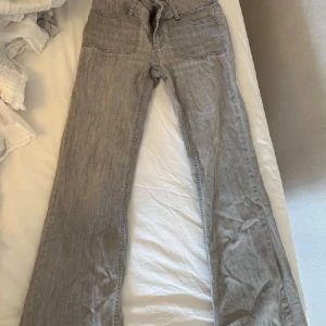 Grå bootcut jeans med fickdetaljer - Snygga grå jeans från Nelly med bootcut passform och låg midja. Jeansen har framfickor och bakfickor med lock och dekorativa knappar. Materialet är klassisk denim i bomull och de har bälteshällor i midjan.