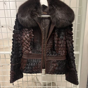 Brun pälsjacka från Punto - Unik brun pälsjacka från Punto med coolt fjällmönstrad yta och bred krage i mörk päls. Jackan har dragkedja framtill och detaljer i mörkbrunt skinn. Perfekt för dig som vill sticka ut med en lyxig och annorlunda look. 