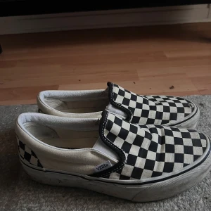 Vans slip-on platform - Klassiska Vans slip-on sneakers med svart och vit rutig checkerboard-mönster. Skorna har en låg profil, platform sula i gummi och är tillverkade i canvas. 