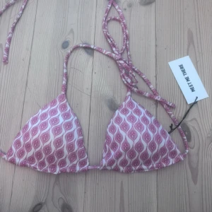 Rosa och vit bikini från Meet Me There - Supersnygg trekantsbikini i rosa och vitt från Meet Me There. Bikinin har ett unikt mönster och smala knytband i nacken och ryggen för perfekt passform. Perfekt för strandhäng.