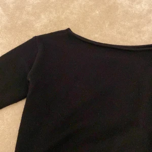 Svart stickad långärmad tröja - Svart stickad tröja med lång ärm och ribbade muddar vid ärmslut och nederkant. Stickad tröja som är lite som en one sholder. Modellen har en enkel,  halsringning och är gjord i ett mjukt stickat material som känns skönt mot huden. Perfekt för dig som gillar stilrena och klassiska plagg. Vet ej vart den är i från, den har ingen lapp.