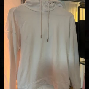 Vit hoodie med huva och snörning - Säljer en stilren vit hoodie med huva och snörning. Tröjan har lång ärm och en klassisk passform, perfekt för chill dagar. Mjuk och skön bomullskänsla, enkel att matcha med jeans eller mjukisbyxor.
