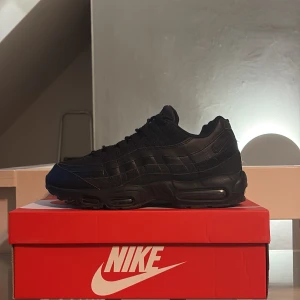 Nike Air Max 95 Essential Svart - Nike Air Max 95 Essential i helsvart. Klassisk chunky siluett med vågformade paneler, synlig Air Max-dämpning och snörning. Köpt för ungefär 1,5 år sedan och har kanske använt dem 10-15 gånger. Skicket är som att dem är helt oanvända men tyvärr finns det en liten slitning i hälen på den högra skon. 