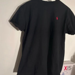 Svart t-shirt från Polo Ralph Lauren - Svart t-shirt från Polo Ralph Lauren med klassisk passform och korta ärmar. T-shirten har en liten röd broderad logga på bröstet och är gjord i mjuk bomull. Perfekt basic med stilren look och rund hals.                                                                                        Pris kan diskuteras.