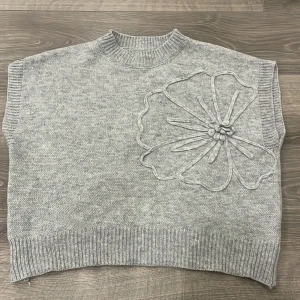 Grå stickad väst med blomdetalj - Snygg grå stickad tröja med en fin blomma! 