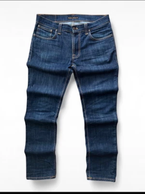 Blå jeans från Nudie Jeans - Mörkblå Nudie Jeans Thin Finn i tvätten Ecru Embo. En ikonisk modell från Nudie Jeans med smal och modern passform, perfekt för en stilren och tidlös look.  Jeansen är i mycket bra skick och har använts väldigt lite. Inga hål, fläckar eller andra defekter. Bekvämt material med lätt stretch som ger bra passform och komfort.  Storlek: W33 / L32 Mått: 1/2 midja: 43 cm Längd: 107 cm Lårbredd: 27 cm Benöppning: 18 cm  Modell: Thin Finn Tvätt: Ecru Embo Färg: Mörkblå Material: 98 % bomull, 2 % elastan