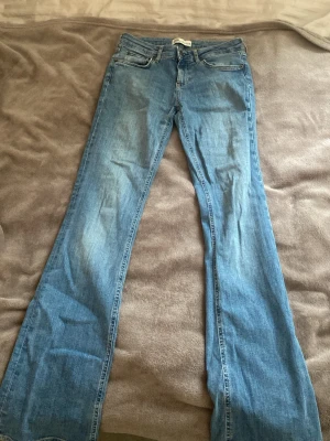 Blå bootcut jeans från Zara, strl 36 - Säljer ett par ljusblå bootcut jeans från Zara i storlek 36. Klassisk femficksmodell med normal passform och utsvängda ben. Jeansen har dragkedjegylf och är tillverkade i mjukt denimtyg som sitter skönt på kroppen.