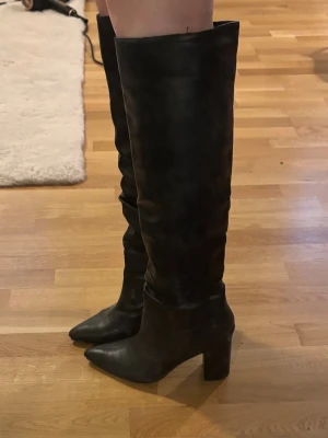 Svarta höga stövlar med klack - Säljer ett par svarta, knähöga stövlar i skinnimitation med spetsig tå och bred klack. 