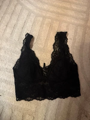 Svart spetsväst från Pieces - Säljer en svart topp/bh Pieces i storlek S. Helt i spets med v-ringad urringning och breda axelband. Perfekt att styla över en topp eller under en kavaj för en trendig look. ❤️‍🔥