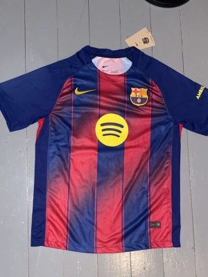 Barcelona tröja Lamine Yamal #10 25/26 - FC Barcelona matchtröja med Lamine Yamal och nummer 10 på ryggen. Tröjan är randig i mörkblått och rött med gula detaljer, Nike-logga och Spotify som sponsor. Tillverkad i polyester med Dri-FIT-teknik för skön känsla. Perfekt för dig som älskar fotboll och Barcelona.