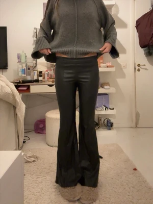 Svarta utsvängda byxor i skinnimitation - Säljer ett par svarta byxor i skinnimitation med utsvängda ben. De har en tight passform upptill och sitter midja till höft. Jag kan tänka mig att diskutera priset 