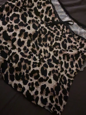 Leopardmönstrad linnetopp med rosett - Snygg topp med leopardmönster i beige, svart och bruna toner. Toppen har tunna axelband, liten rosett framtill och spetskant längs urringningen. Materialet är mjukt och följsamt, perfekt för en trendig look.